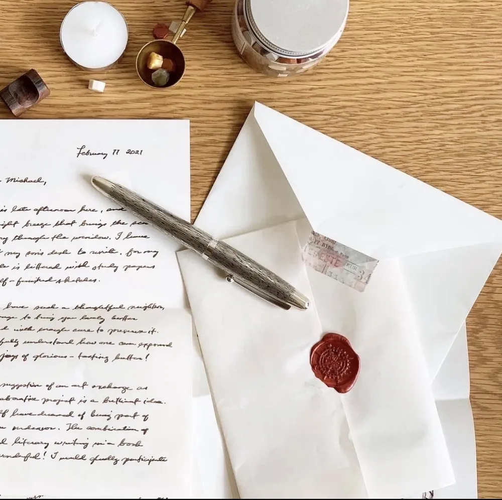 A finished handwritten letter and fountain pen beside a white envelope closed with a red wax seal